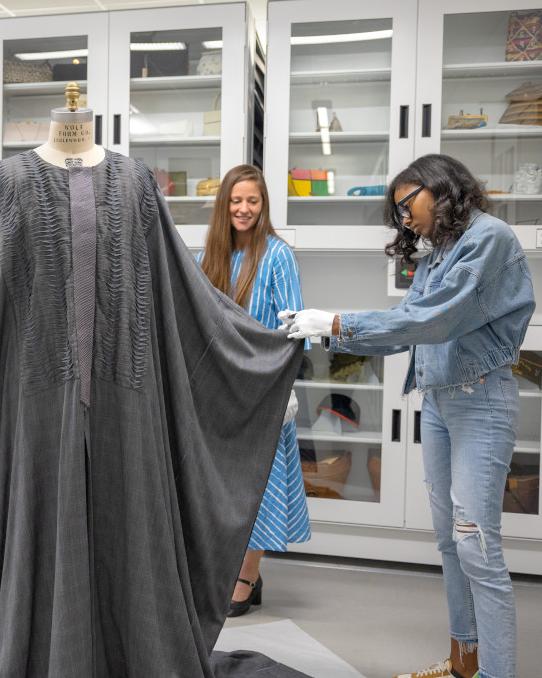 professor and college students examining a caftan on a mannequin