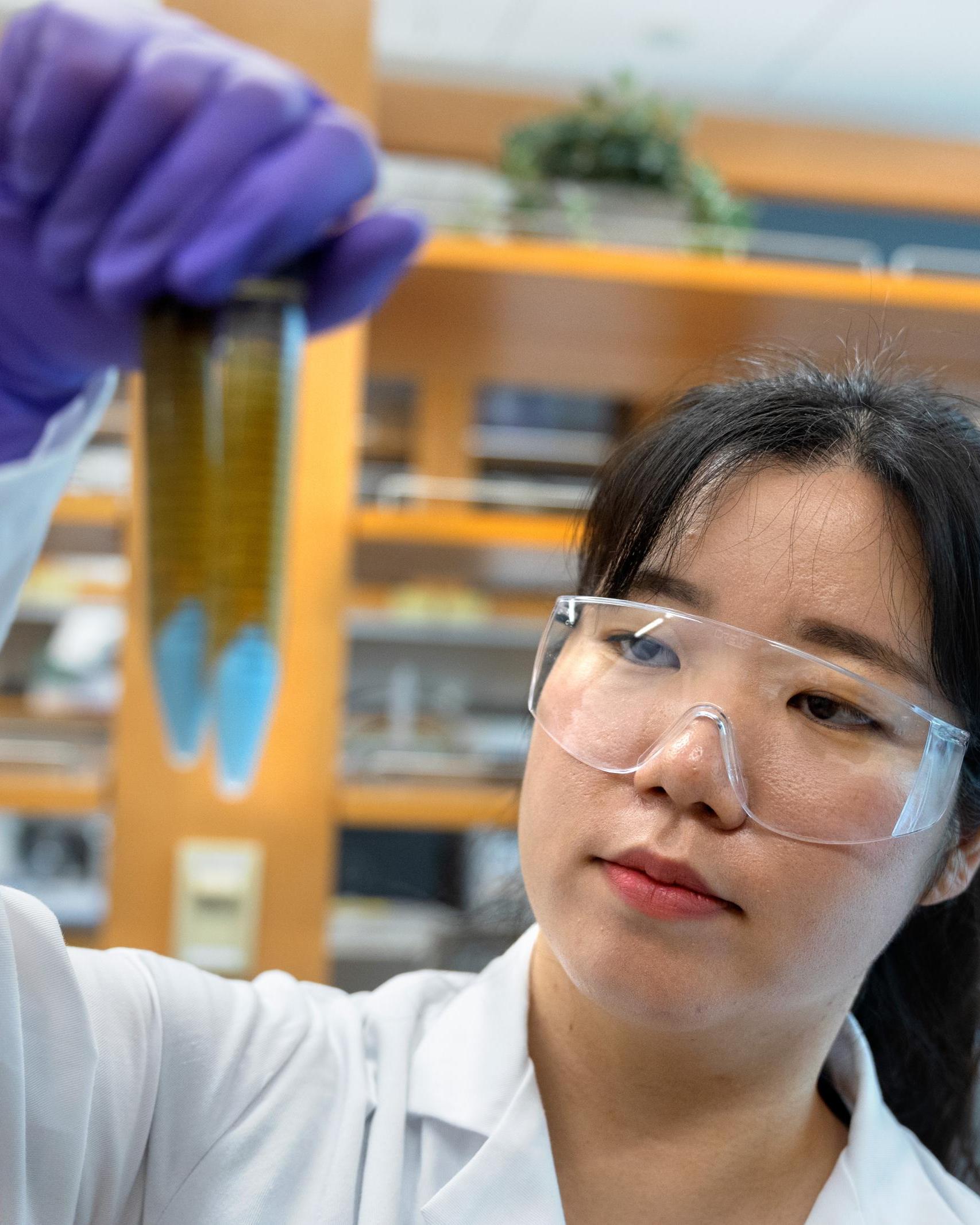 graduate student in goggles and a lab coat holds up vials