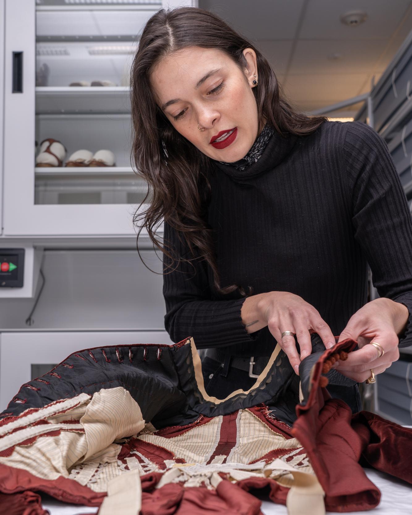 person touching a historical garment on a table