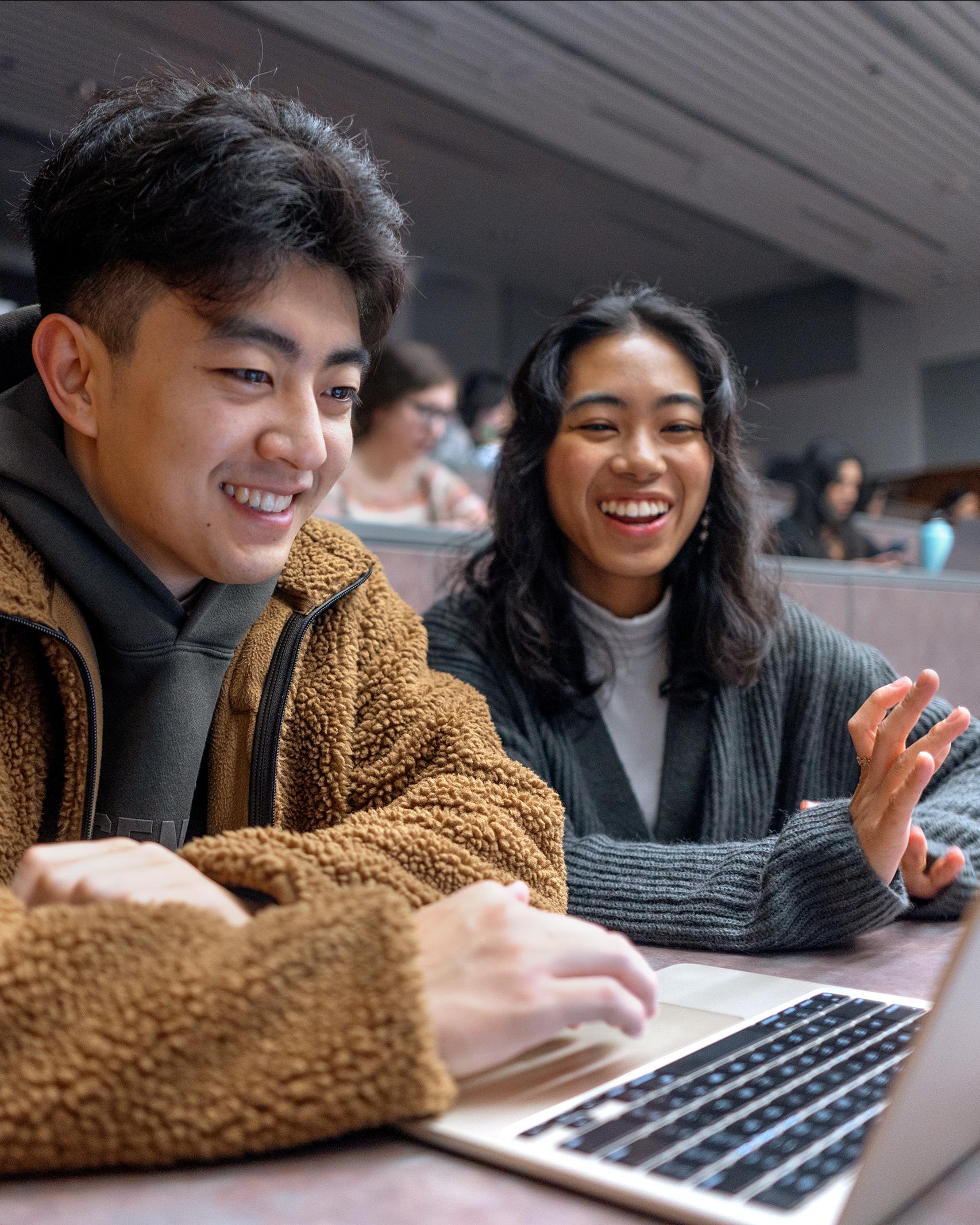 two college students in class smiling at a laptop