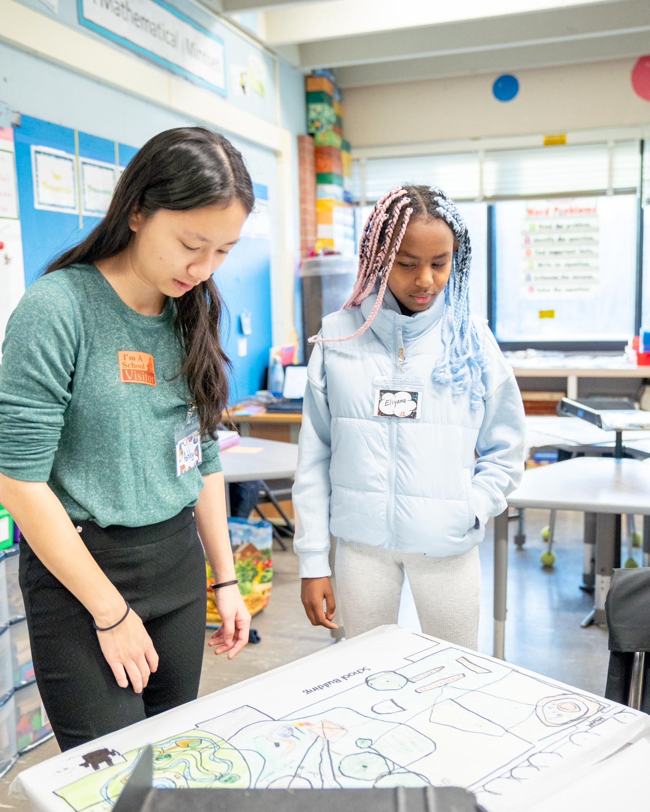graduate student looks at plans with a fifth grader in a classroom