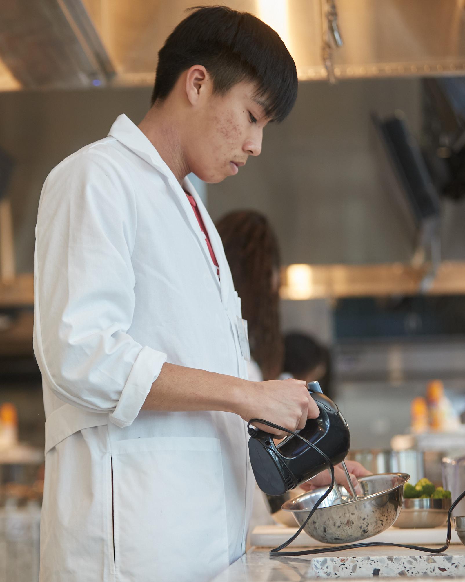 college student using a hand mixer in a professional kitchen