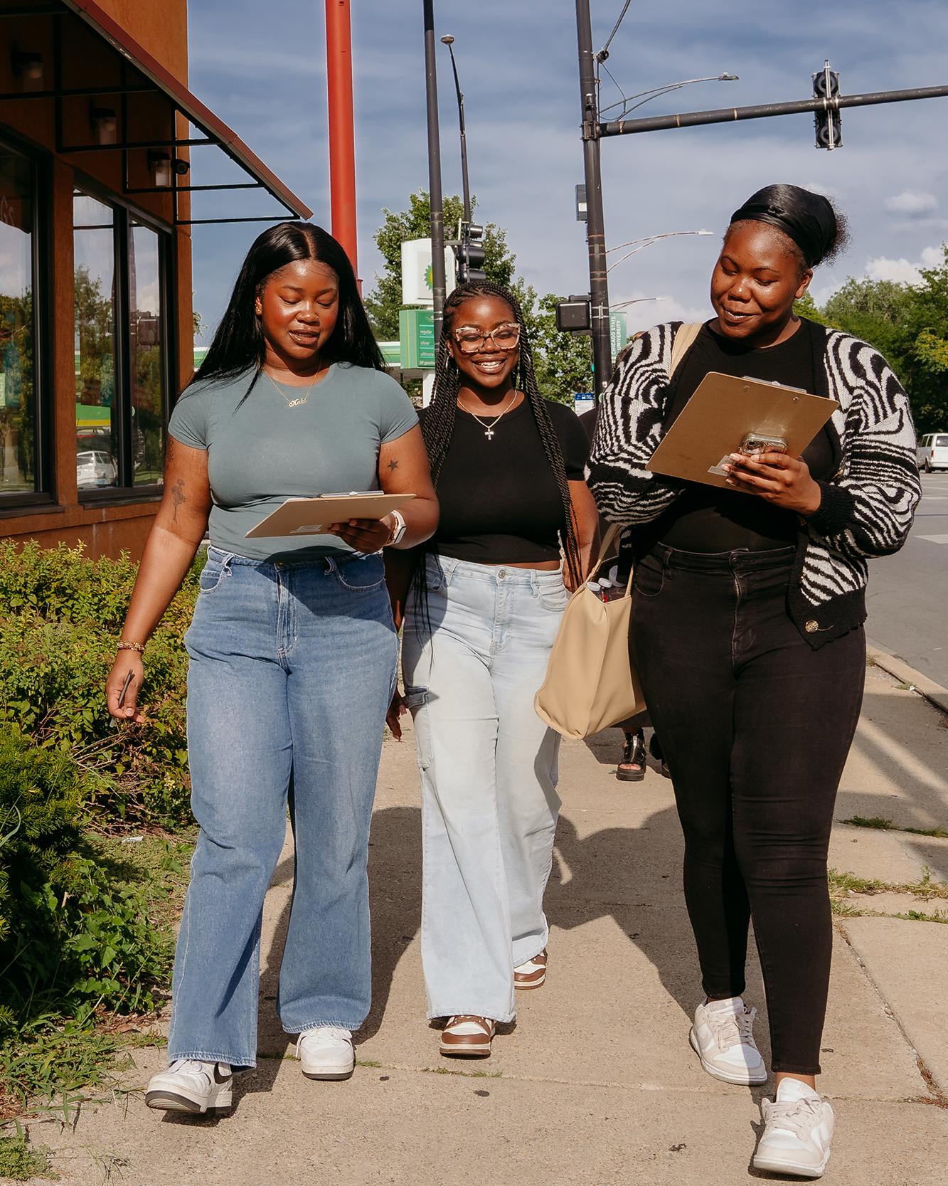 three college students walking down a city street with clipboards
