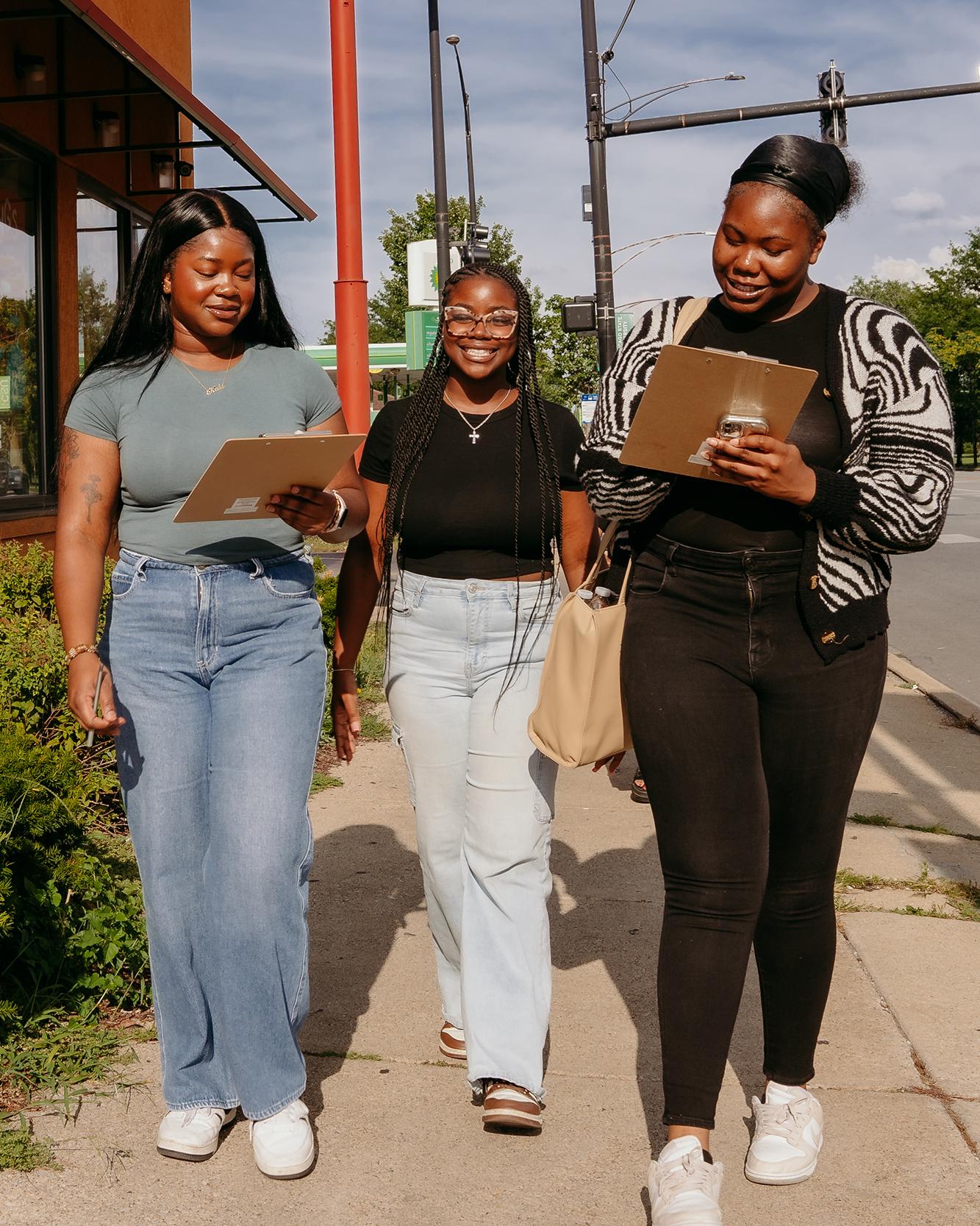 three college students walking down a city street with clipboards