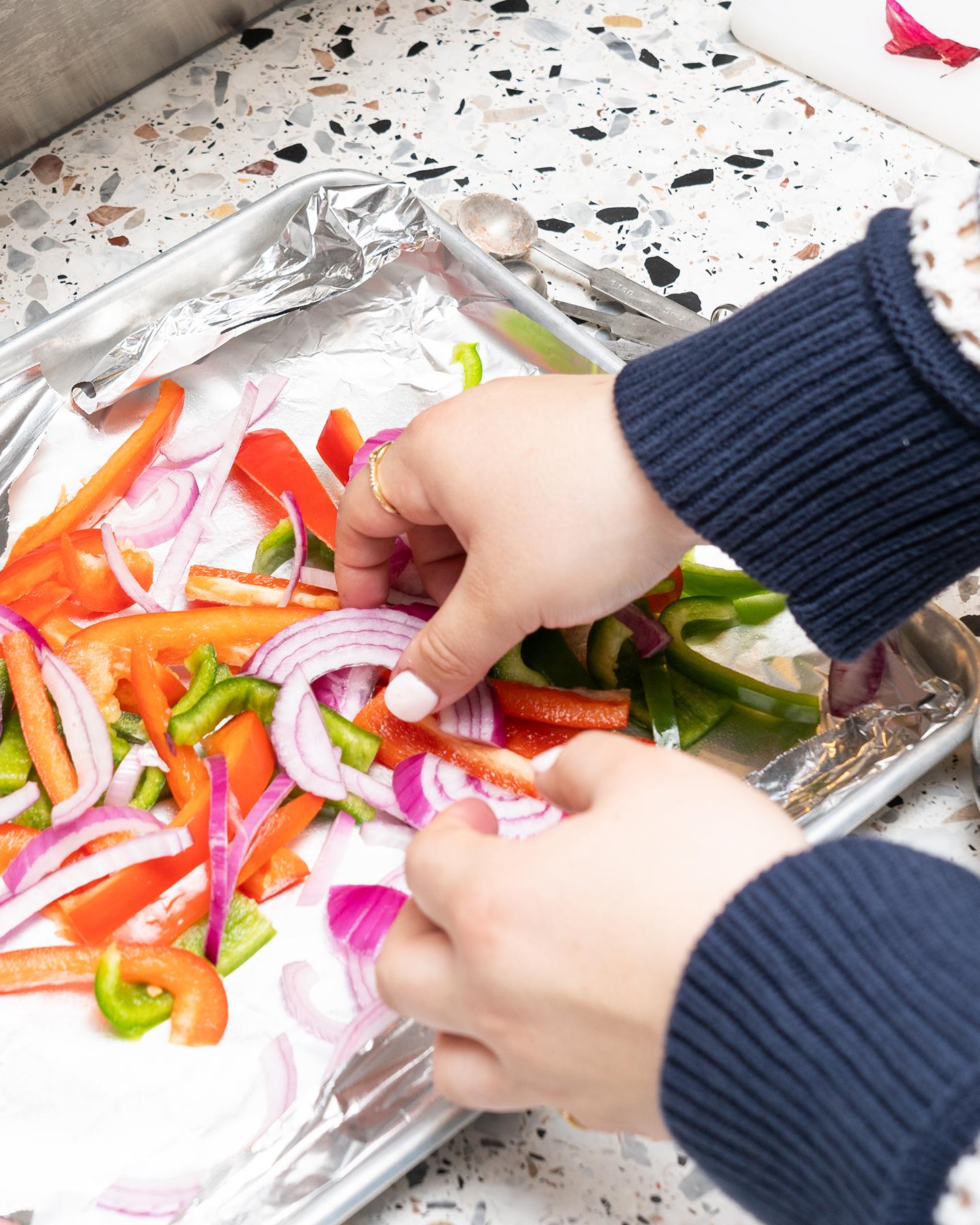 hands placing sliced vegetables on a baking tray