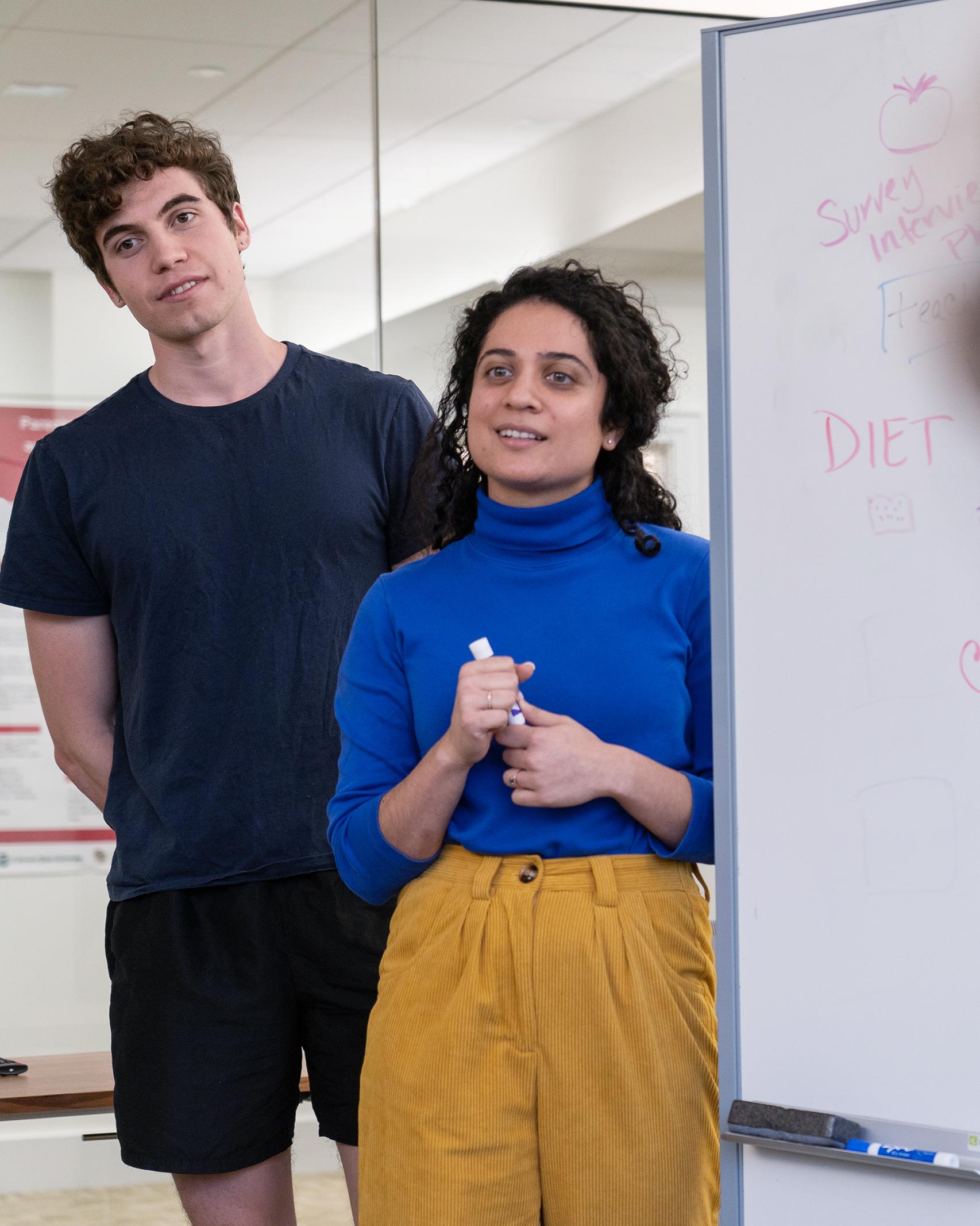 two college students stand next to a whiteboard
