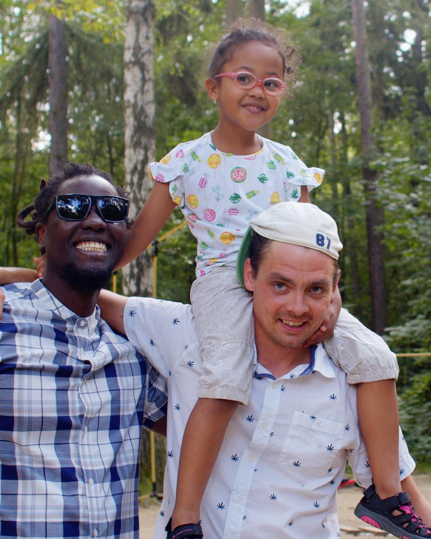 two fathers, one with a young girl on his shoulders, in a park