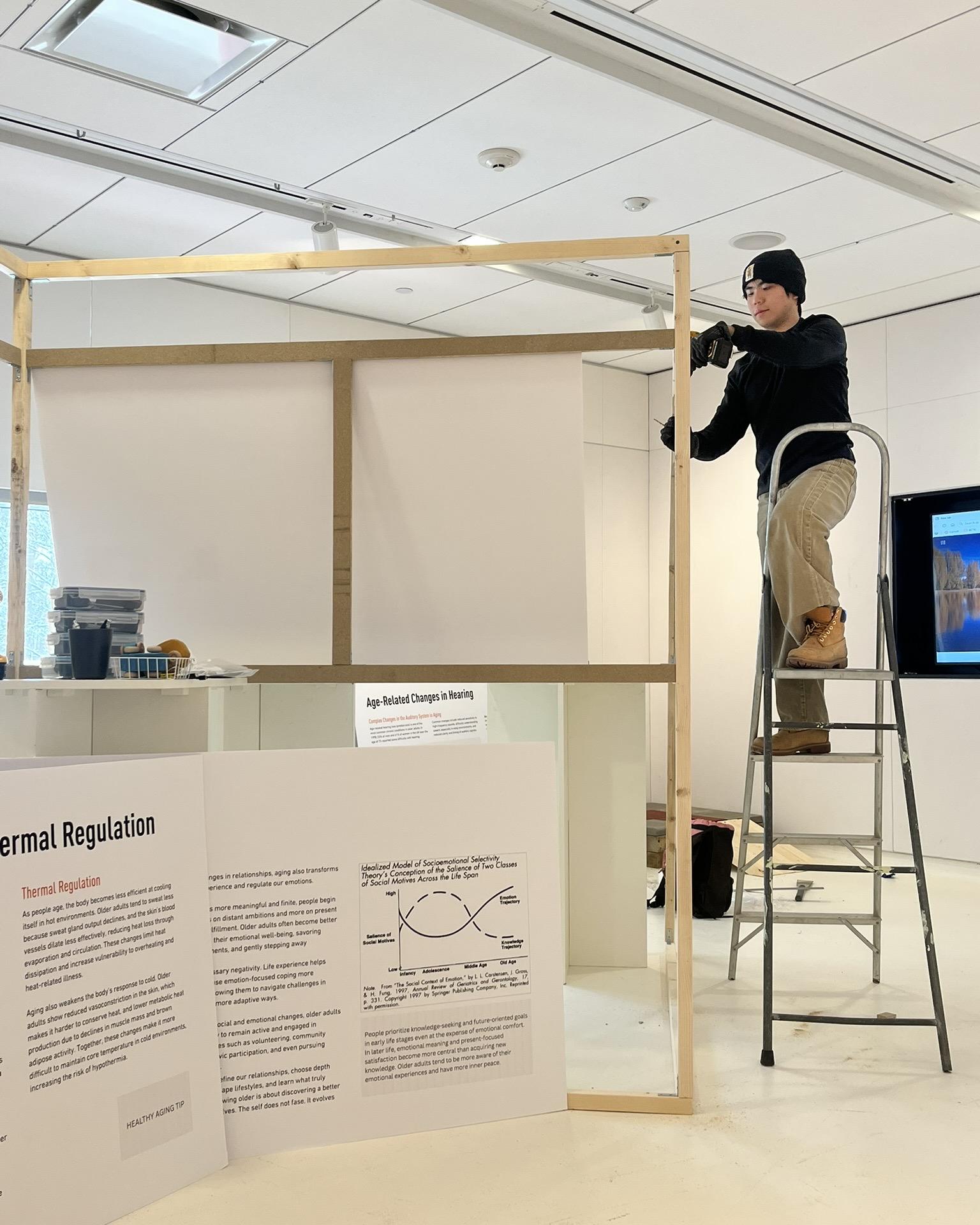 Ruizen Wang on a ladder building the exhibit 