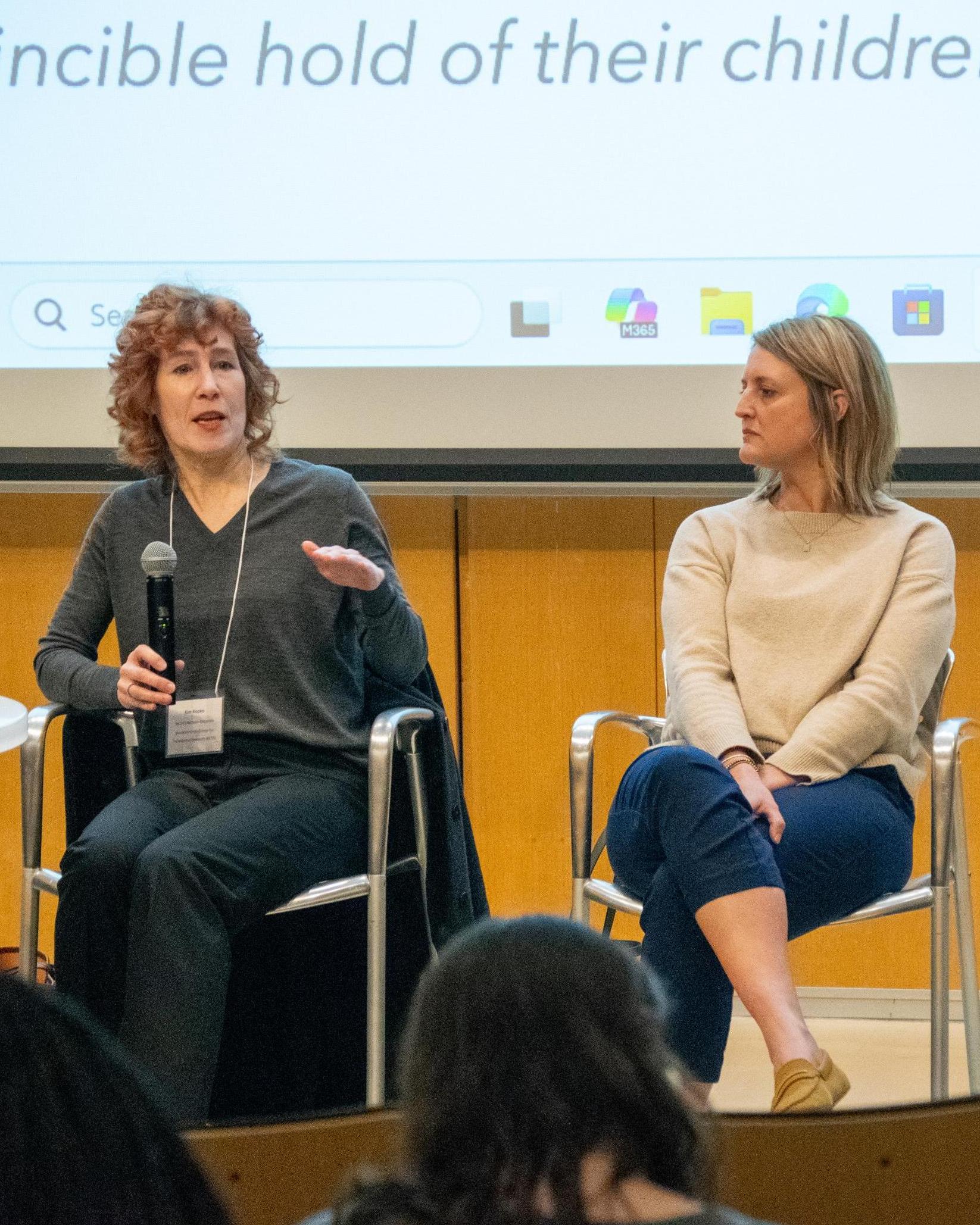 Two people in front a room speaking, one with a microphone