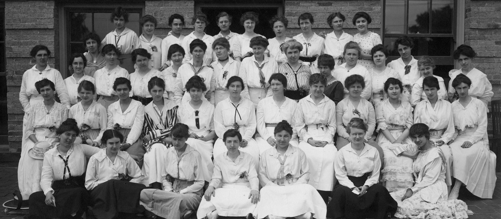 group of about 60 women in white outfits sitting in rows in the 1920s