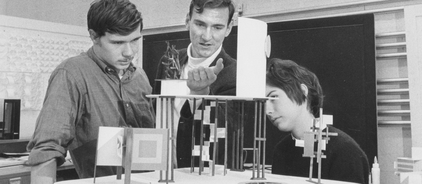 Three students examining 3-D wooden designs in a studio