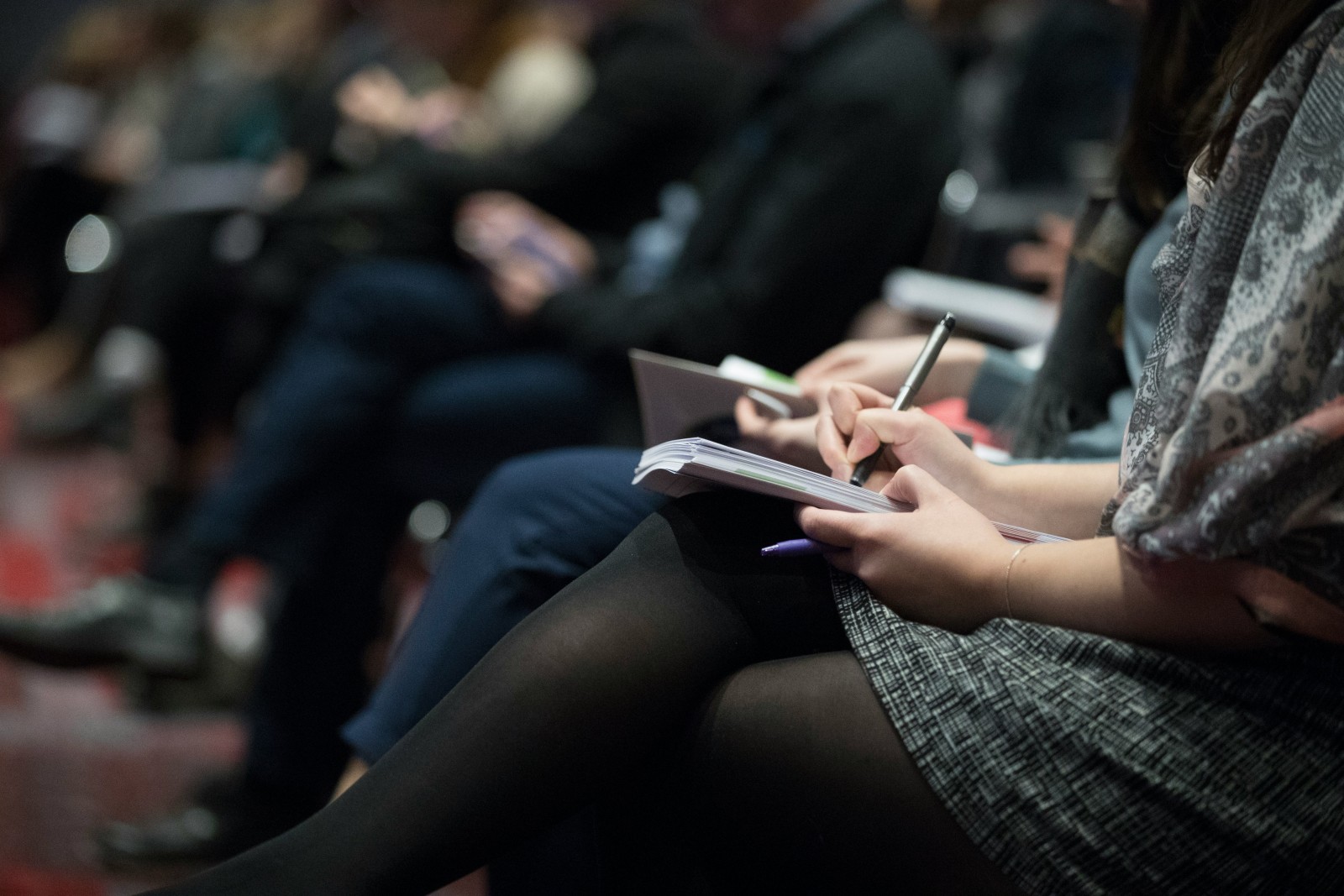 image of sitting people's torsos and legs, several people resting notebooks on their laps