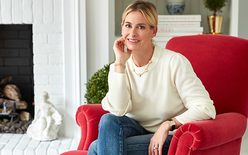 Gwen Whiting sitting in a red chair in front of a bookcase and fireplace