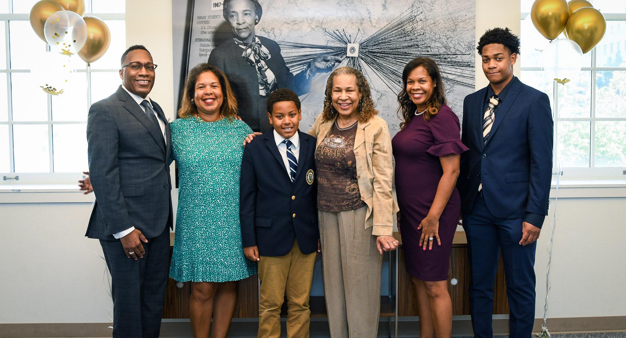 Six members of the Kittrell family stand in front of a portrait of Flemmie Kittrell.