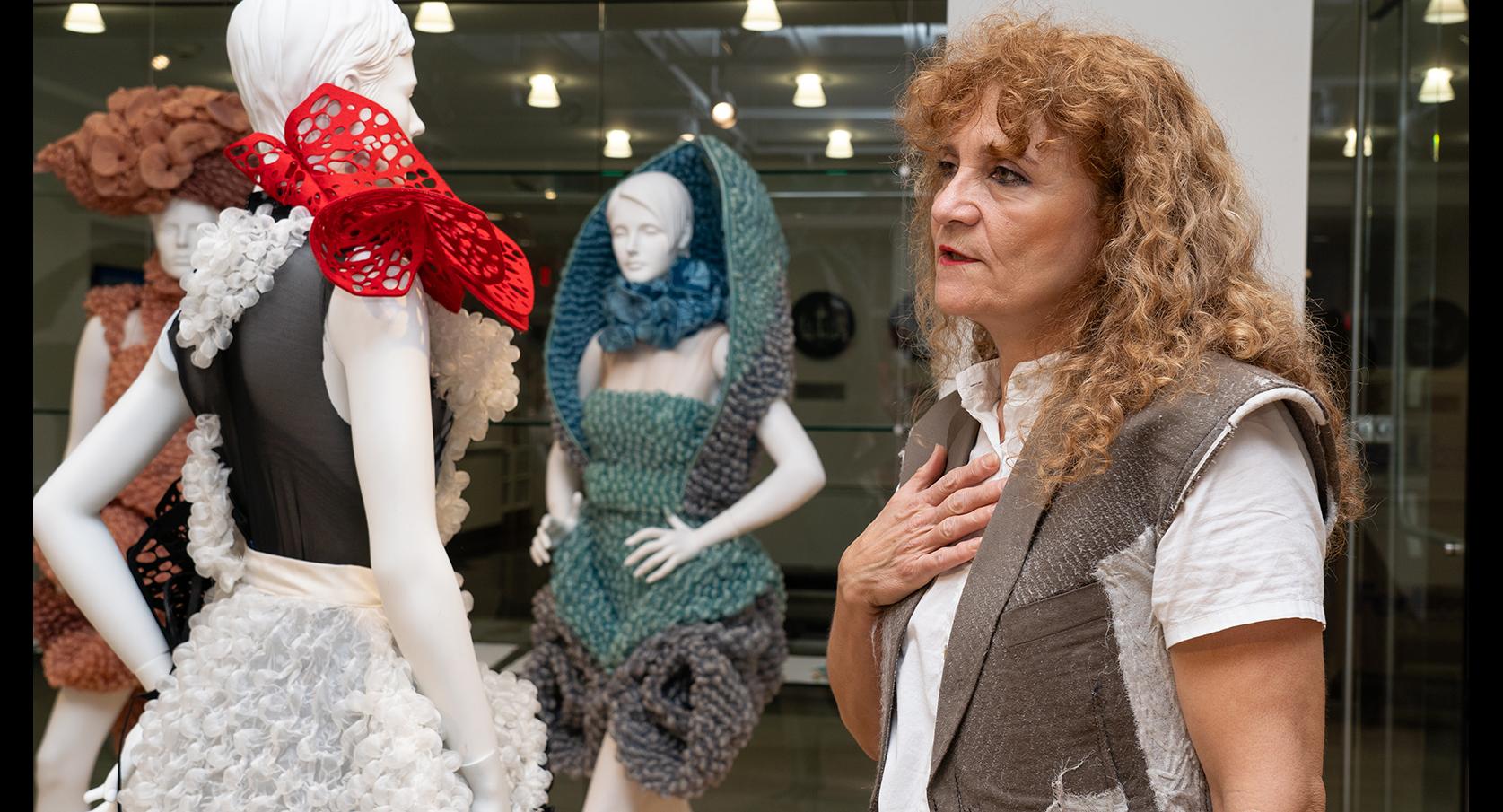 Mihaleva in a gallery with her clothing designs on mannequins behind her