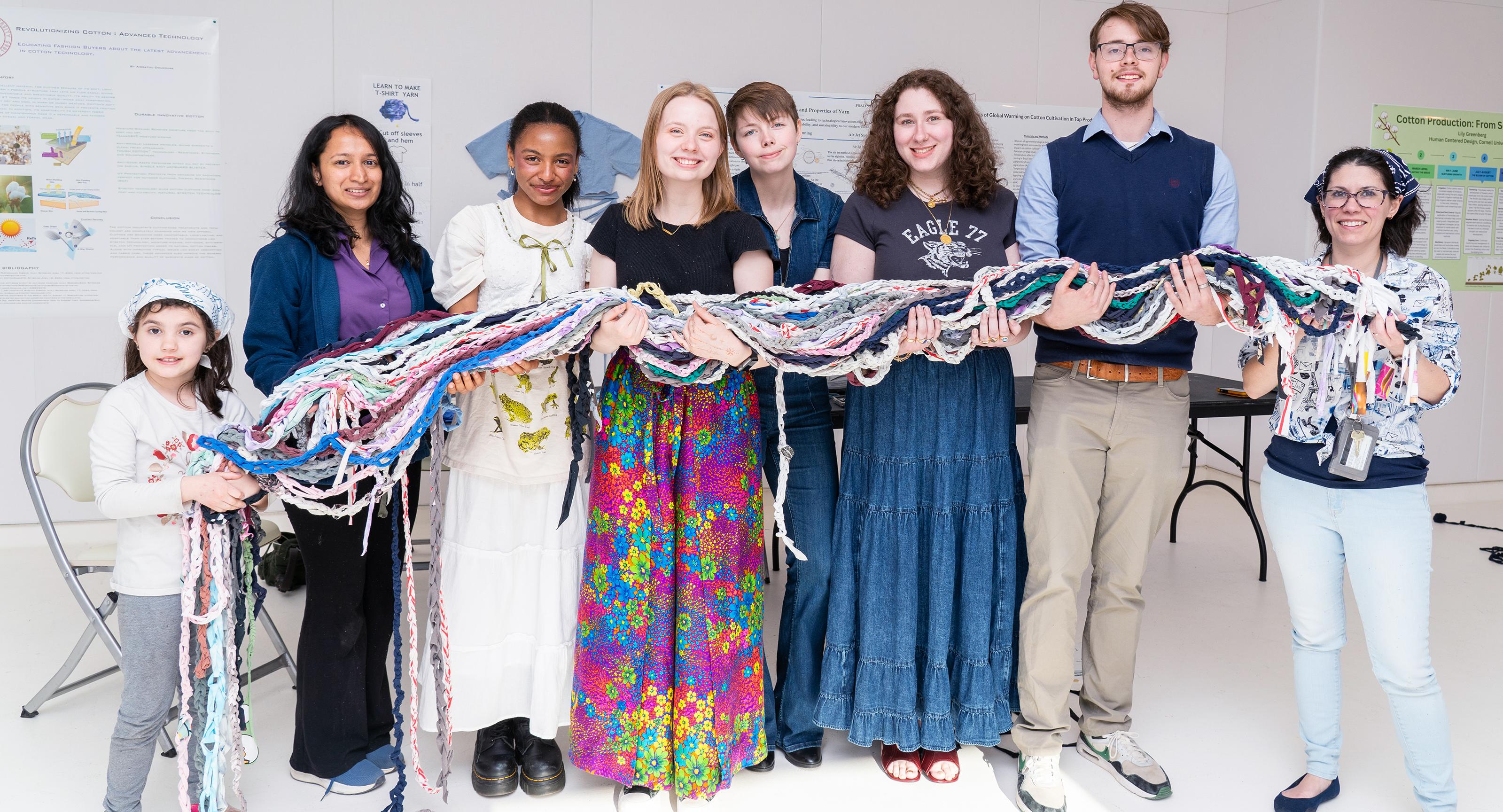 line of college students and professors hold a long rope of woven cotton fabric