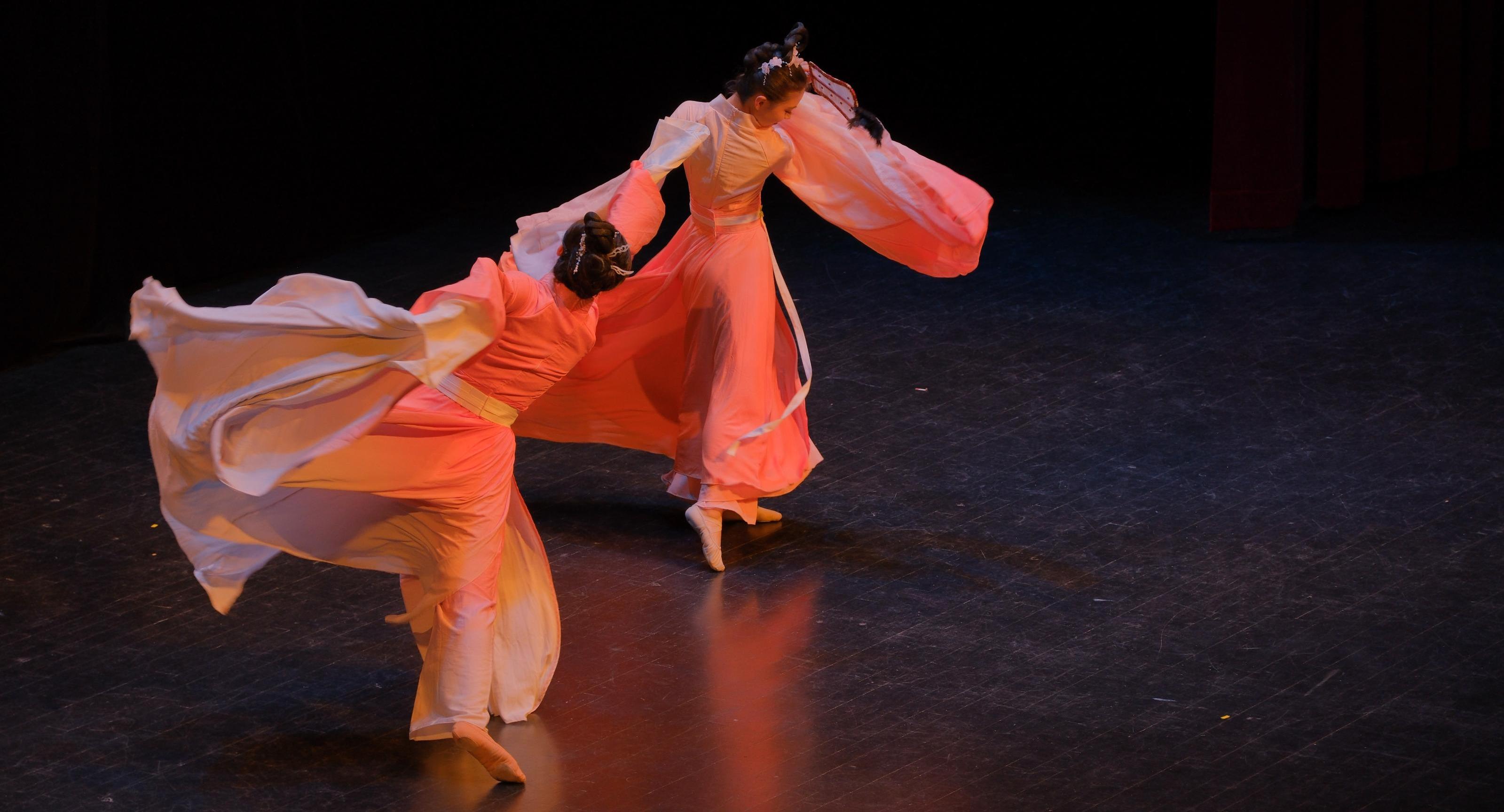 Two students dance in flowing peach outfits