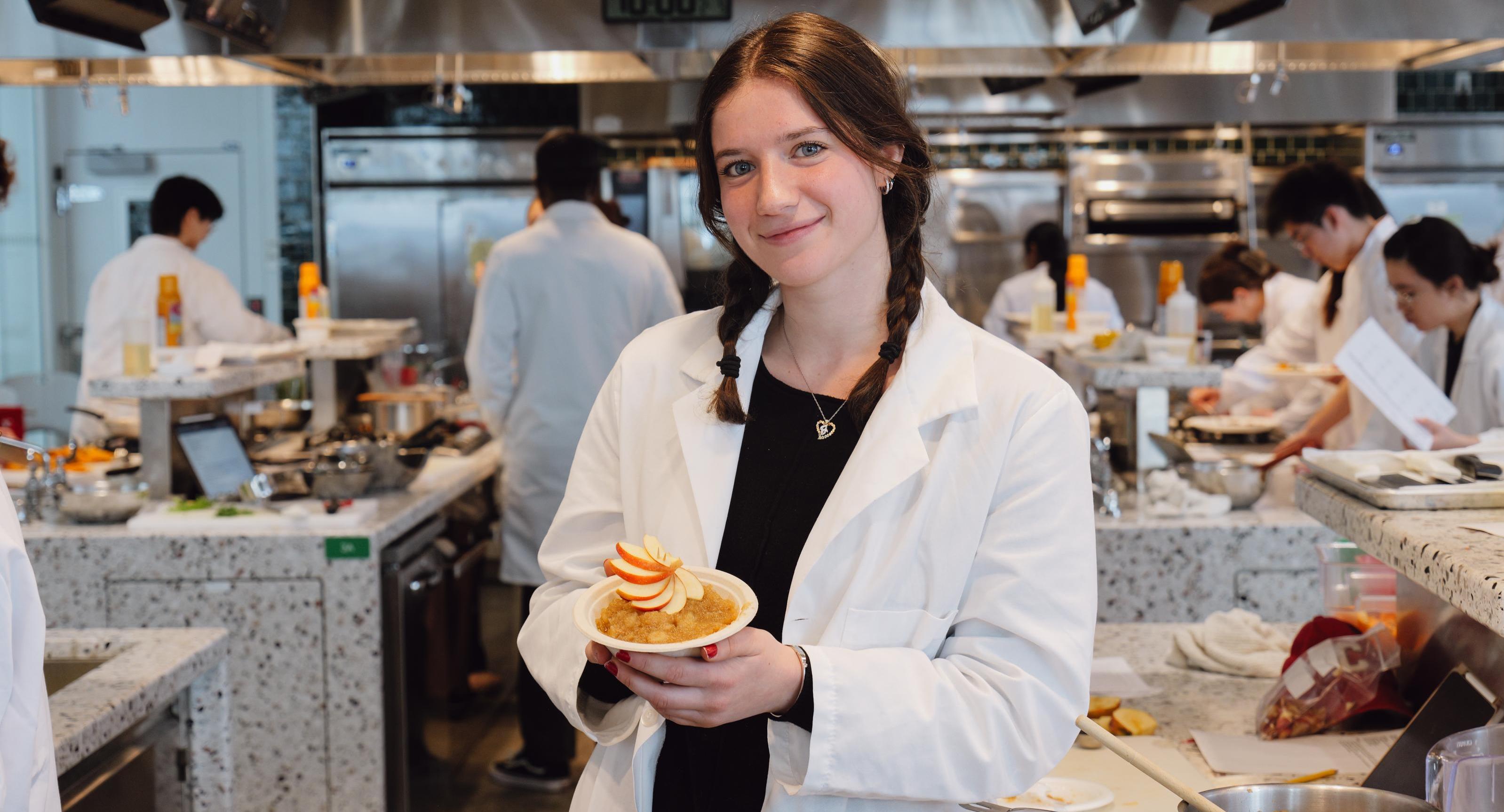 A student poses with the applesauce dish she made in the Discovery Kitchen. 