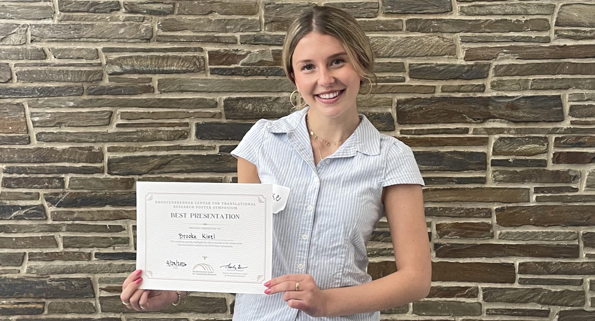 A woman stands in front of a stone facade holding a certificate