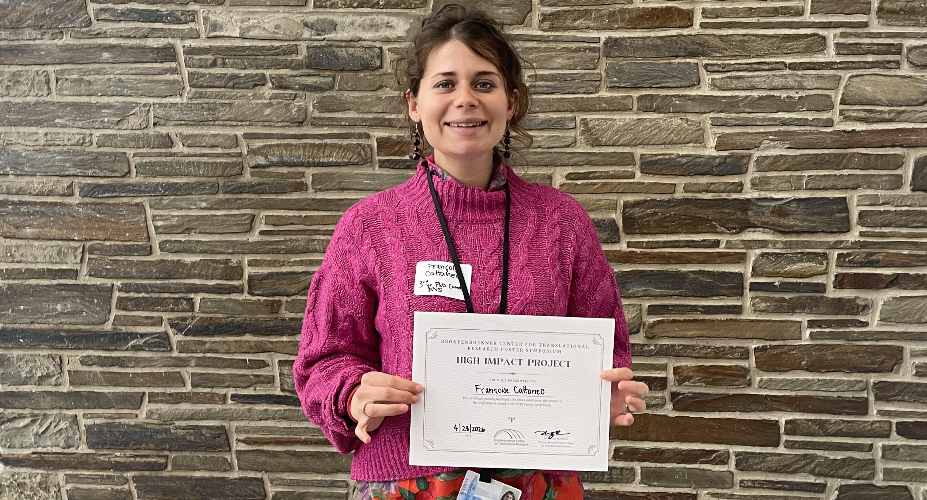 A woman stands in front of a stone facade holidng a certificate