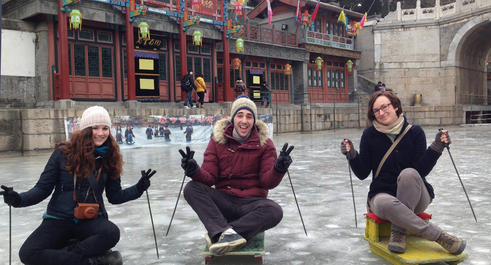 Three people sitting on sleds pushing around the ice in China.