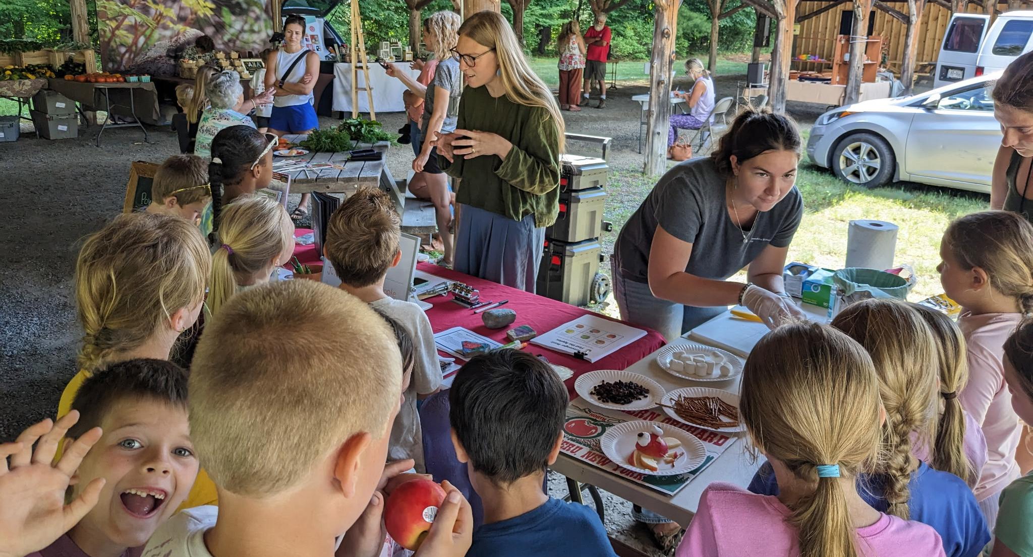 Two volunteers teach kids to make owls out of an apple.