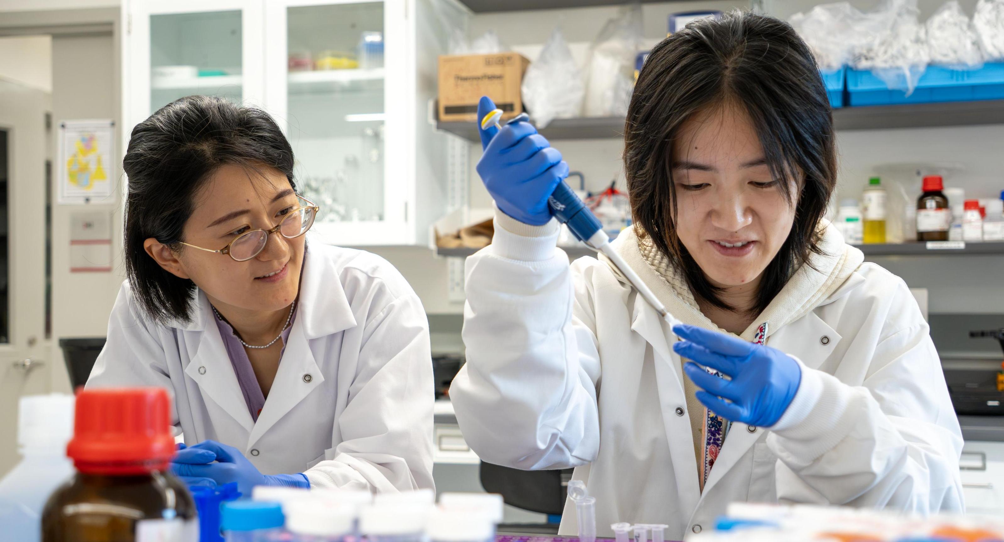 A graduate student pipetting alongside her advisor in a lab. 