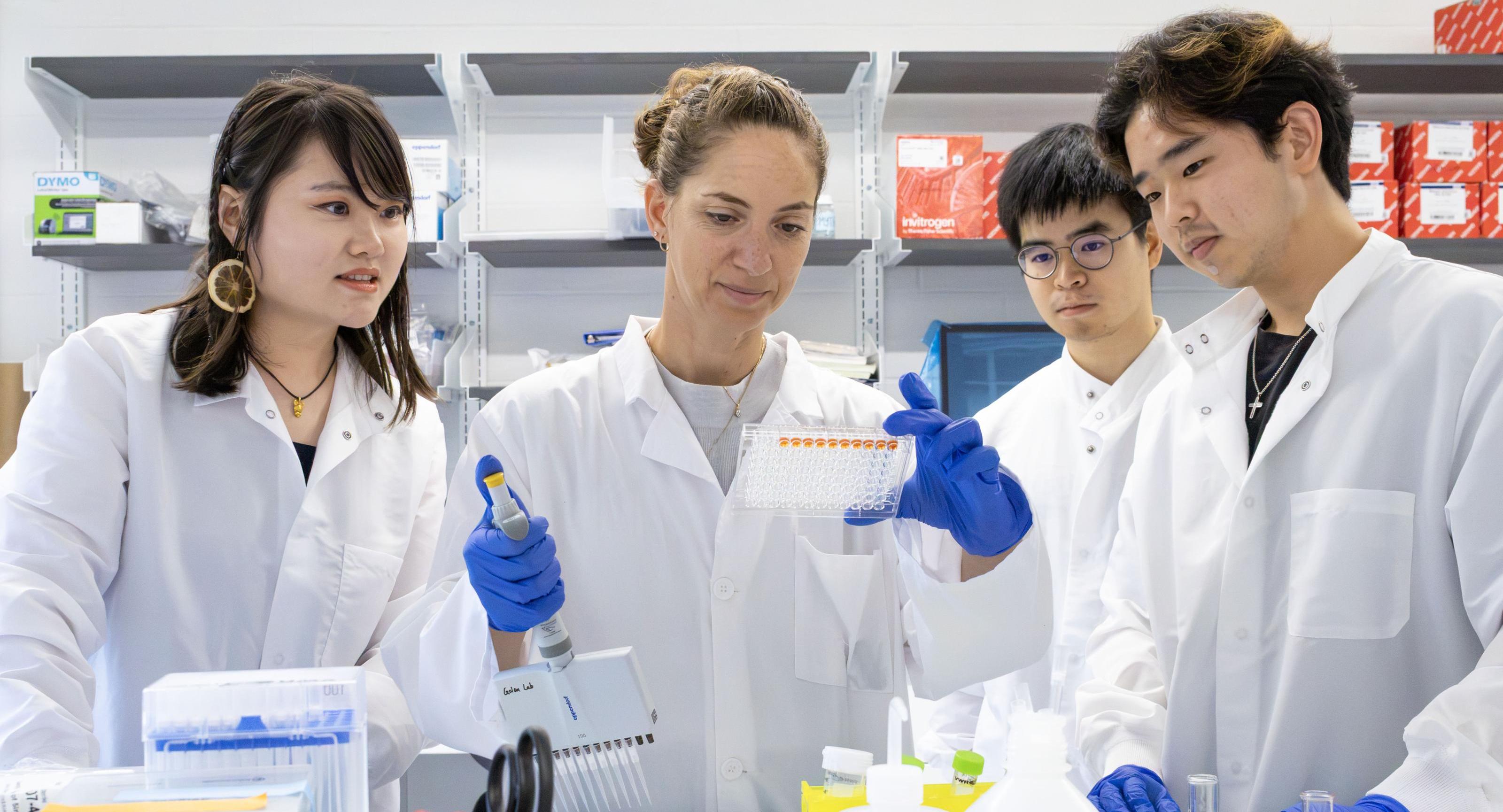 A faculty member holding up a sample surrounded by students in a lab. 