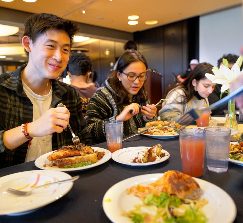 students sitting at a dining hall table eating a meal