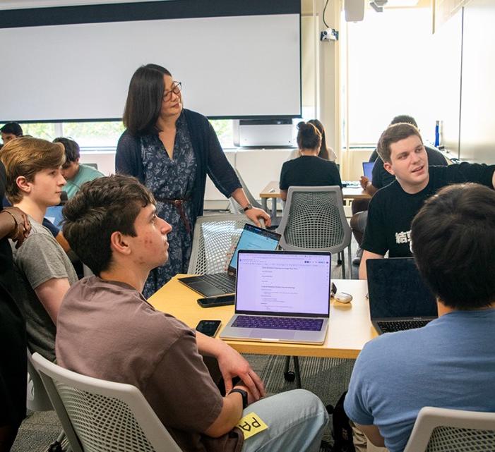 group of adults and teens sit at a table and look at writing on a white board