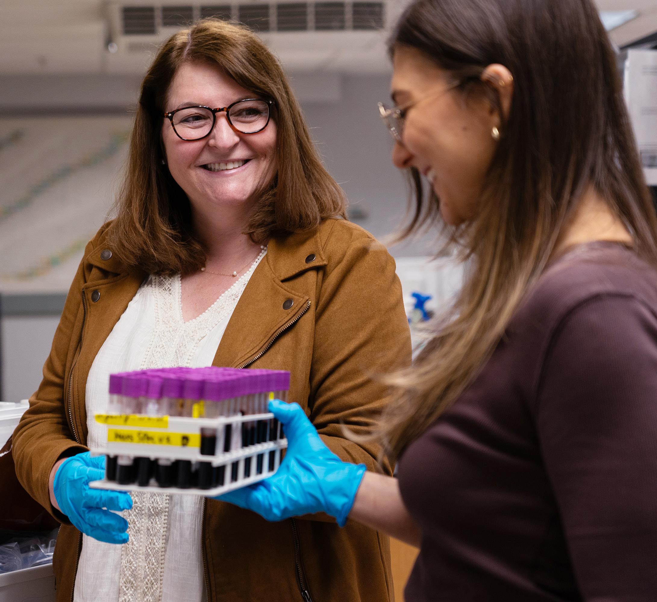 woman in glasses receives a tray of vials from a student in a research lab