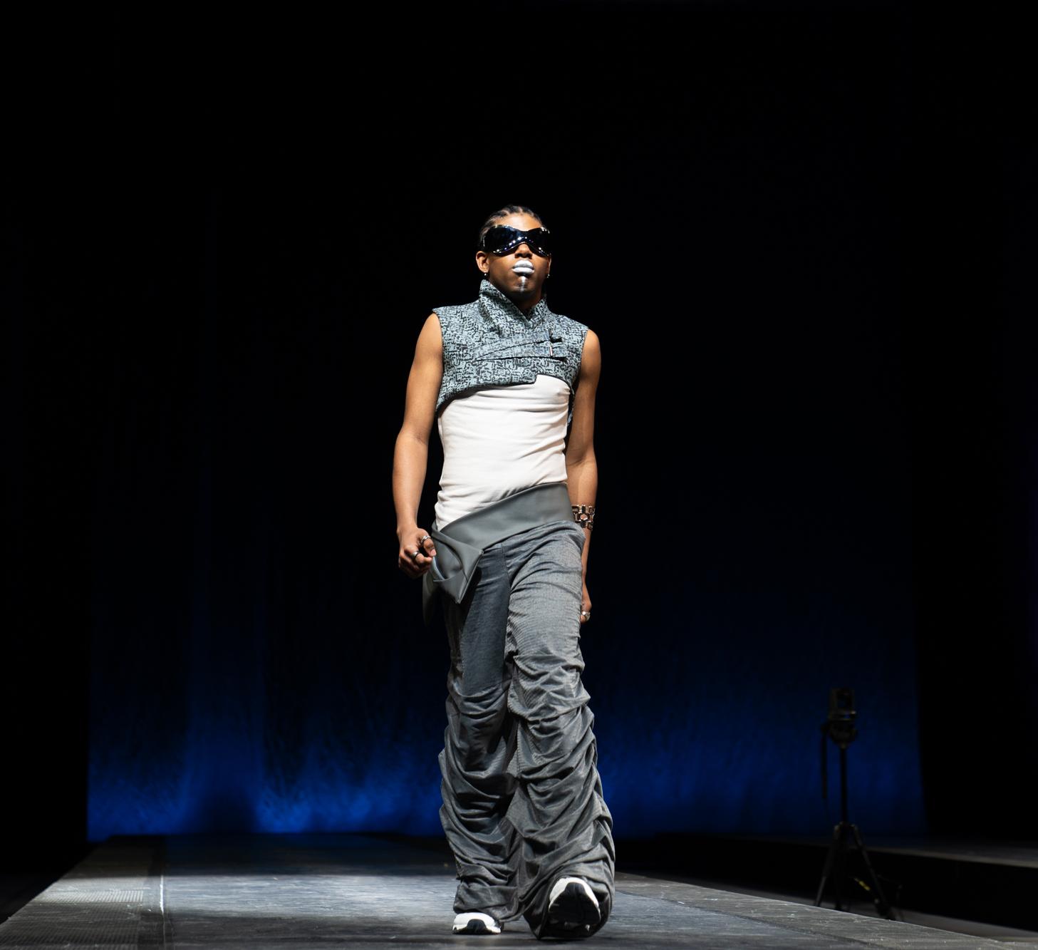 person in pants, t shirt and shrug walks the runway