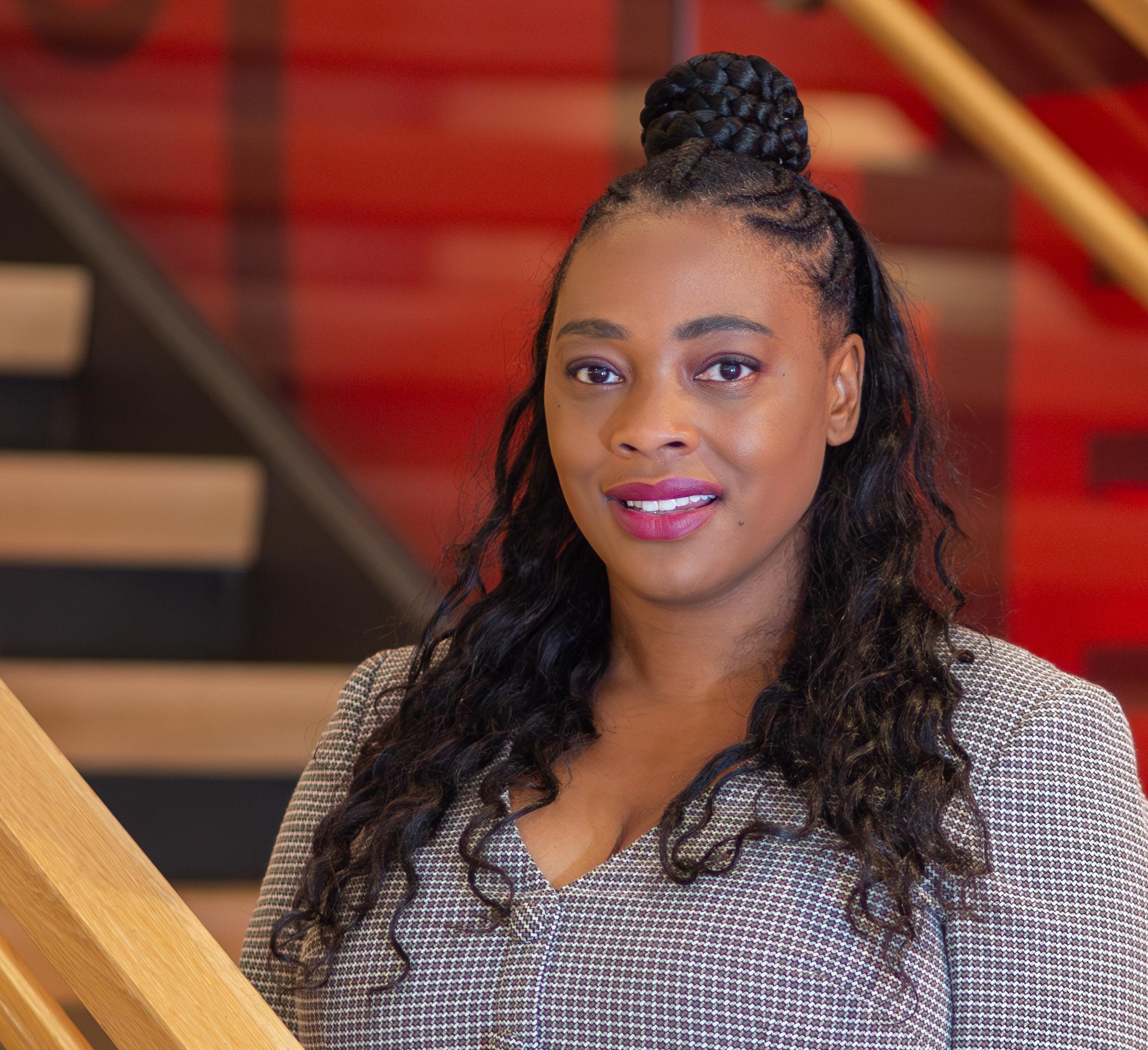 Woman in grey dress standing with a red wall behind her
