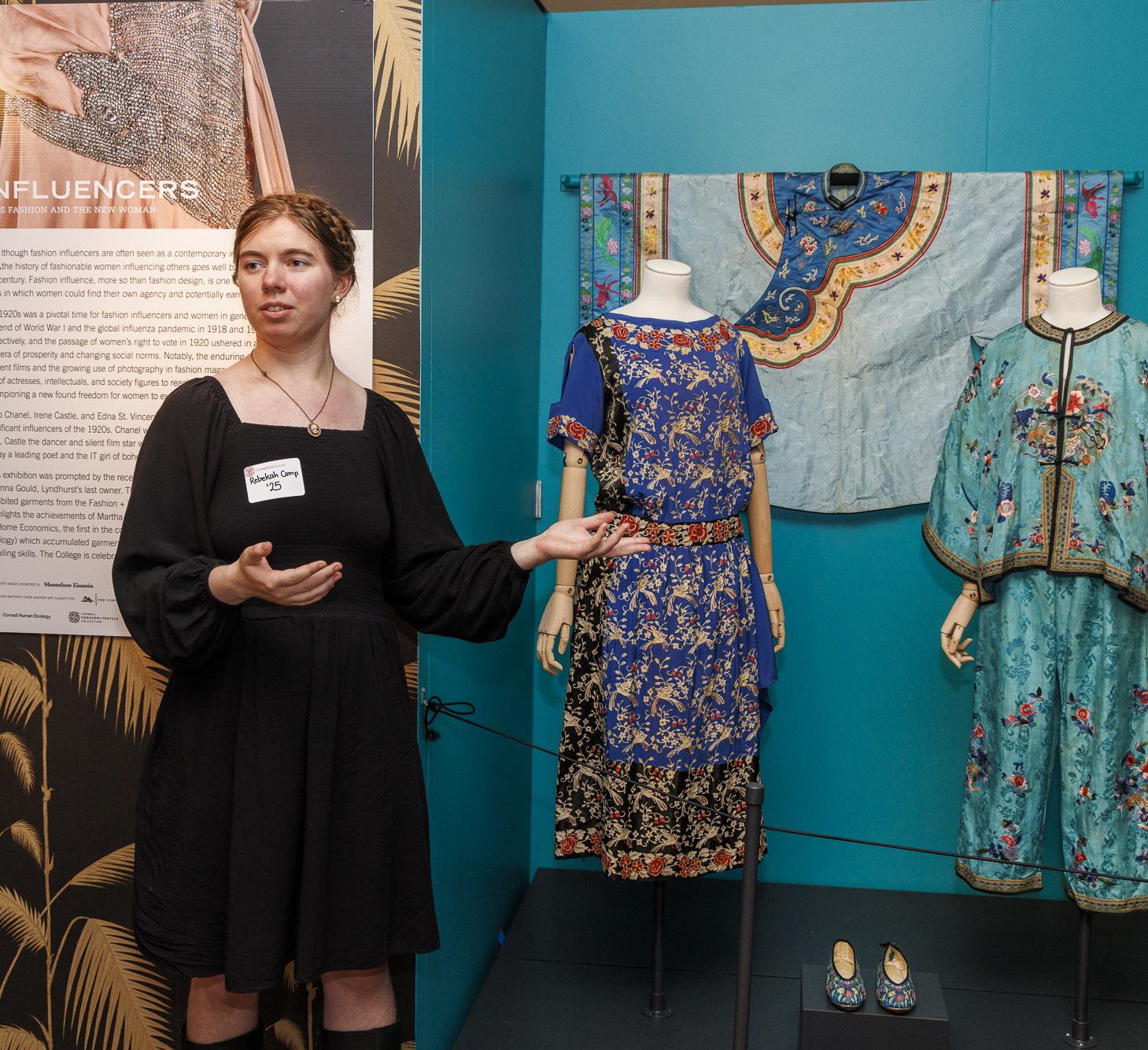 student gestures at some vintage dresses on mannequins in an exhibition