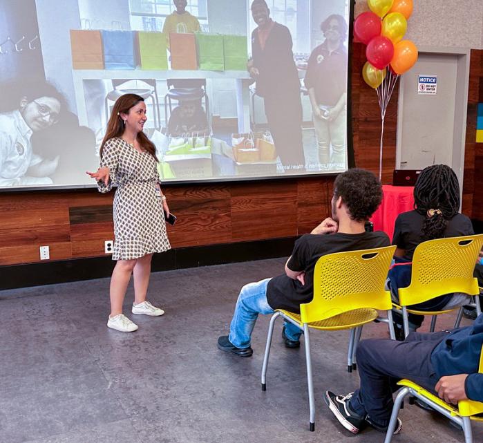 young woman speaking in front of youth seated in yellow chairs