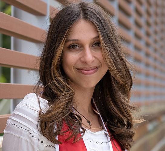 Isabelle Ilan wearing a white blouse and the Cornell stole standing in front of a wooden wall