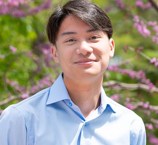 Aidan Collins wearing a blue shirt and smiling outside.