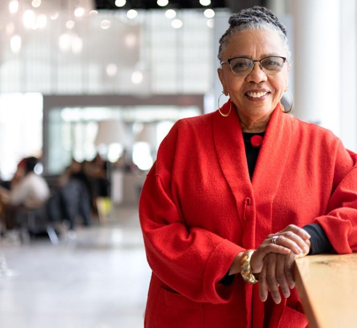 Woman in a red coat leans on a counter and smiles