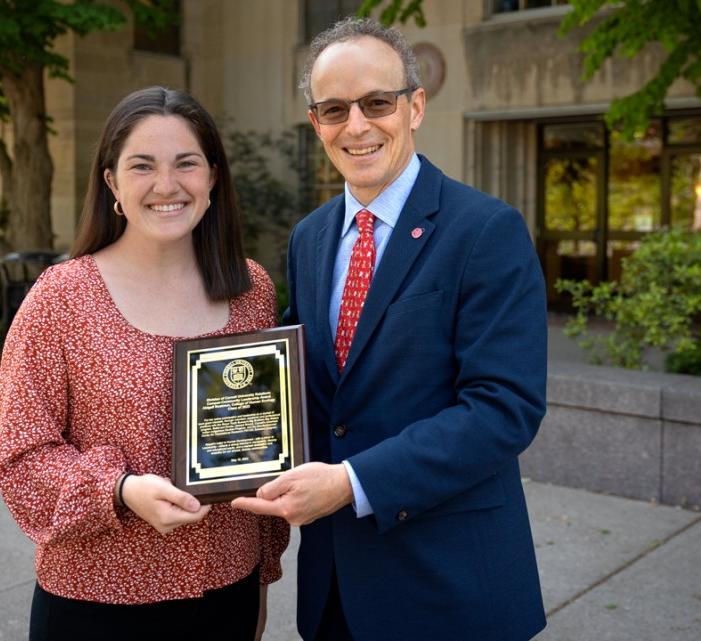 undergraduate student receiving a plaque from a man in sunglasses and a blue suit