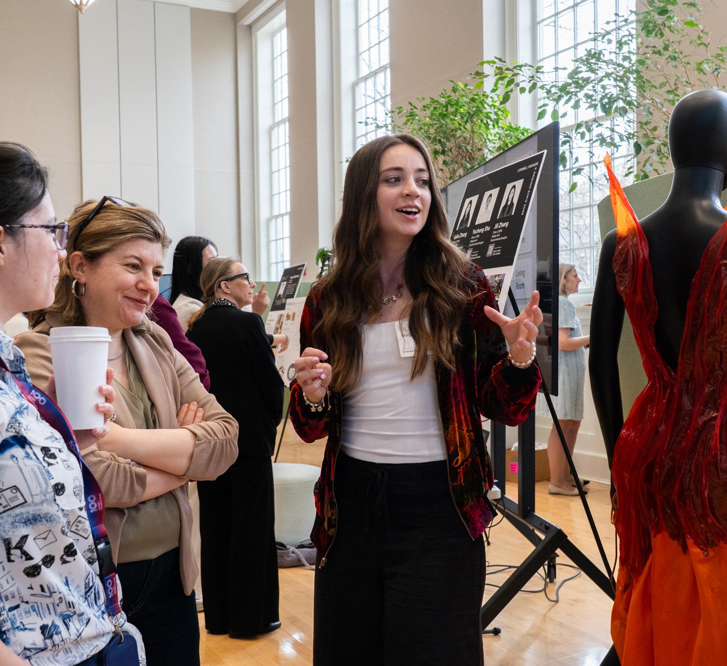 A student gestures toward a mannequin wearing a dress from her collection