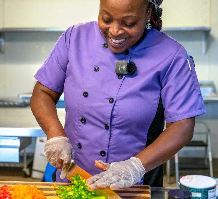 A woman chops peppers in a purple chef jacket