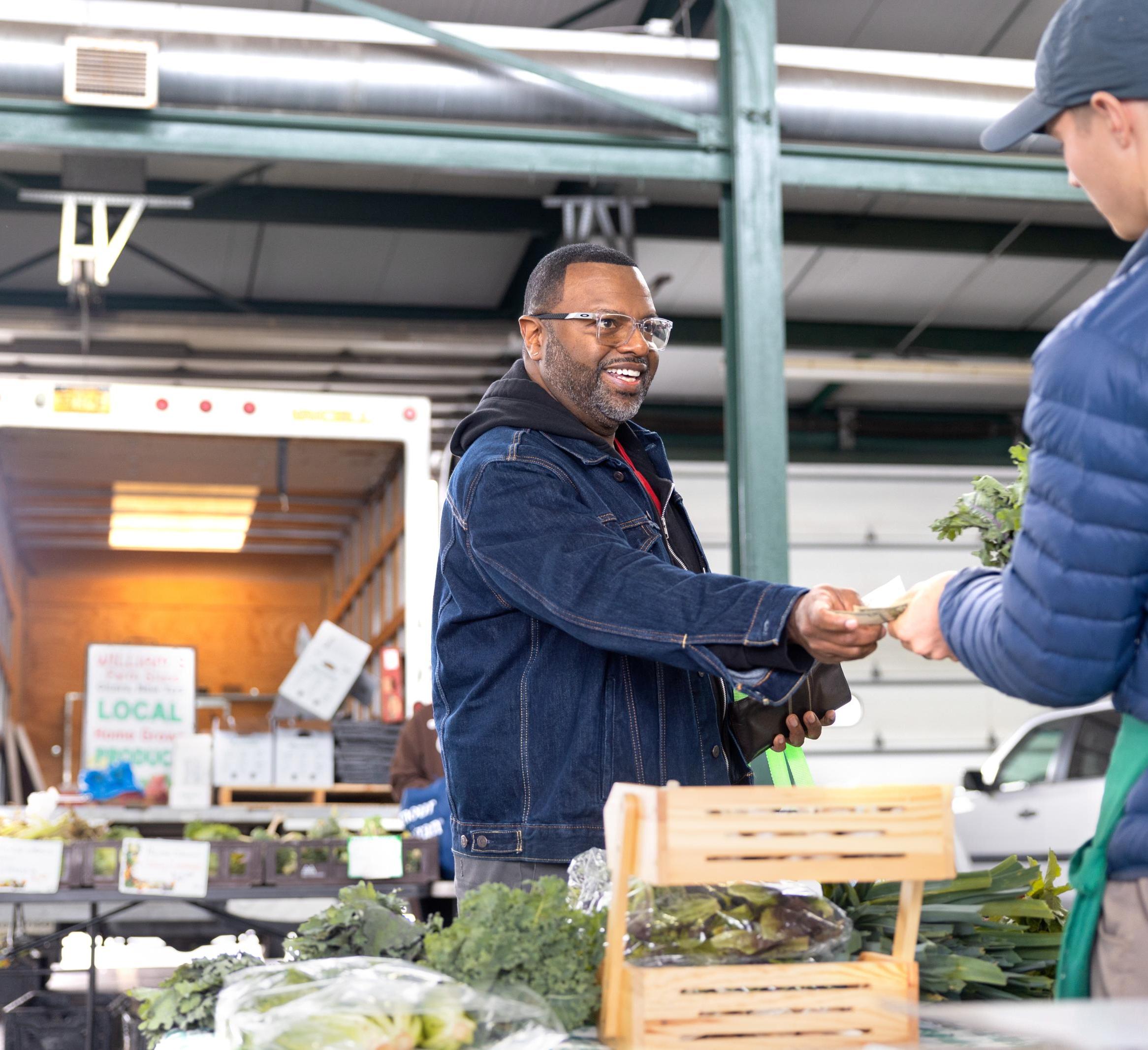 A person hands a SNAP coupon to a farmer