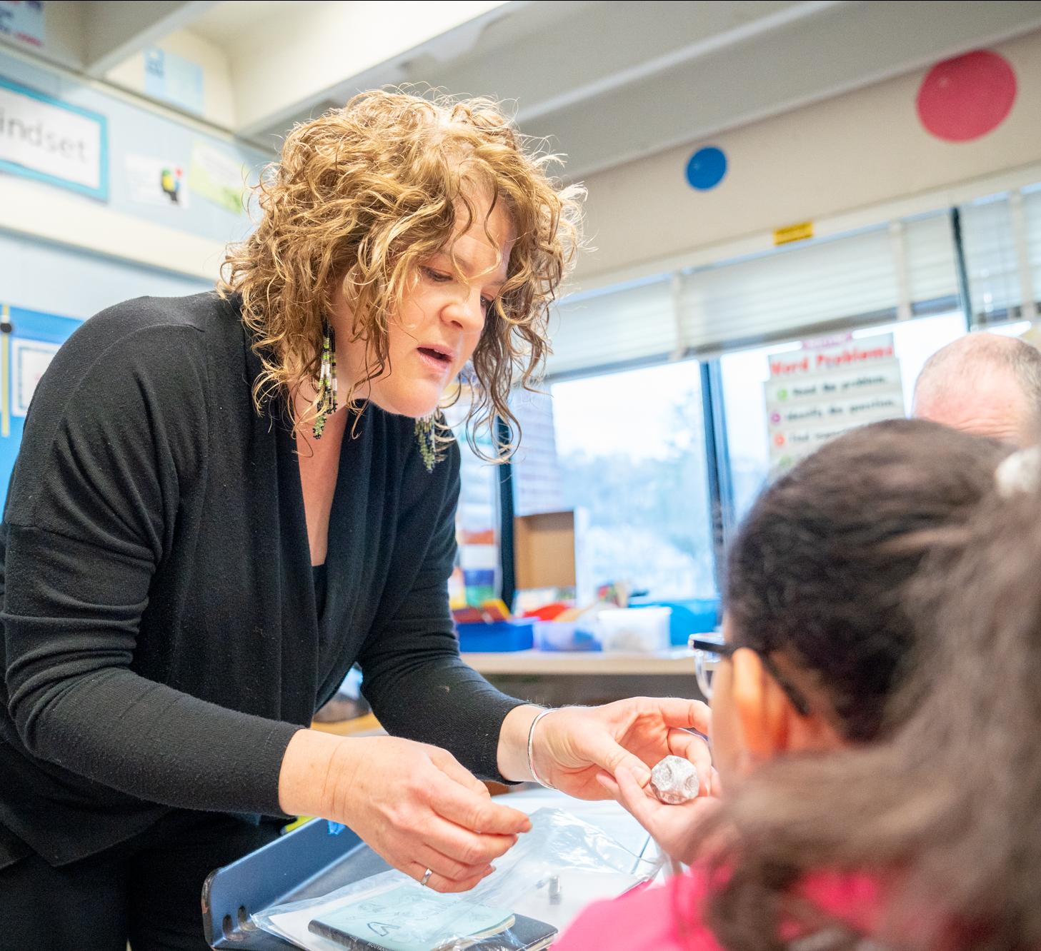 woman leans to talk to elementary school children in a classroom