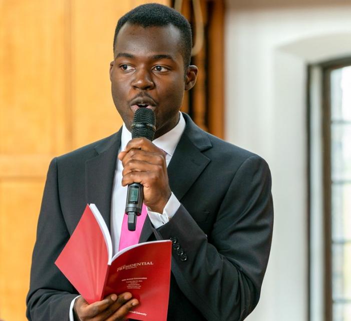 a student speaks into a microphone holding a red booklet