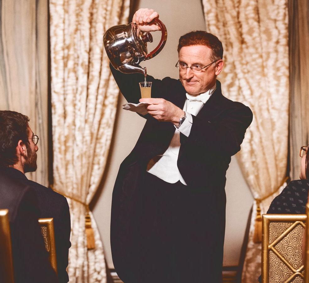 A magician pours liquid into a tiny cup