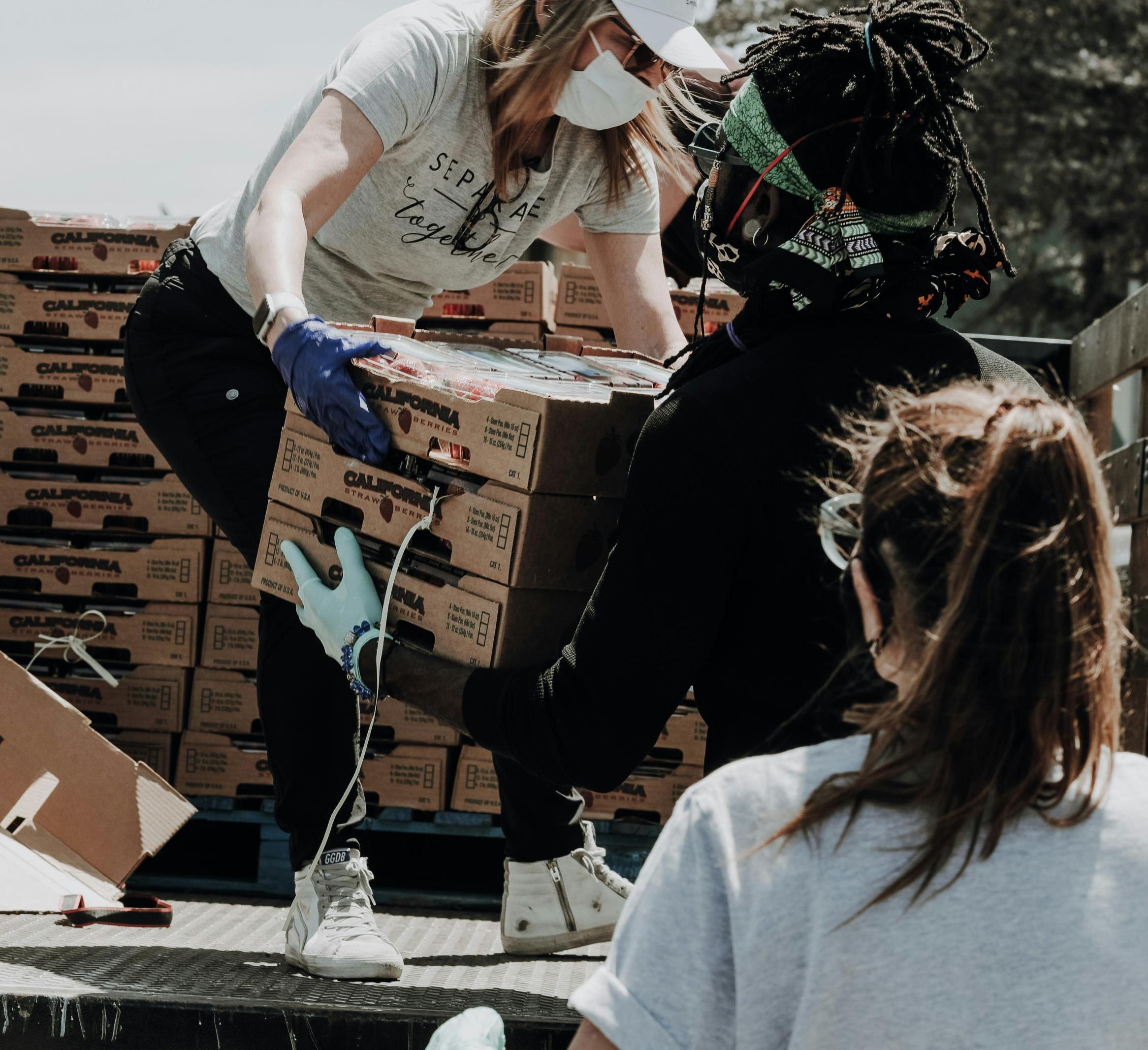 A person hands cases of food to volunteers on a truck 