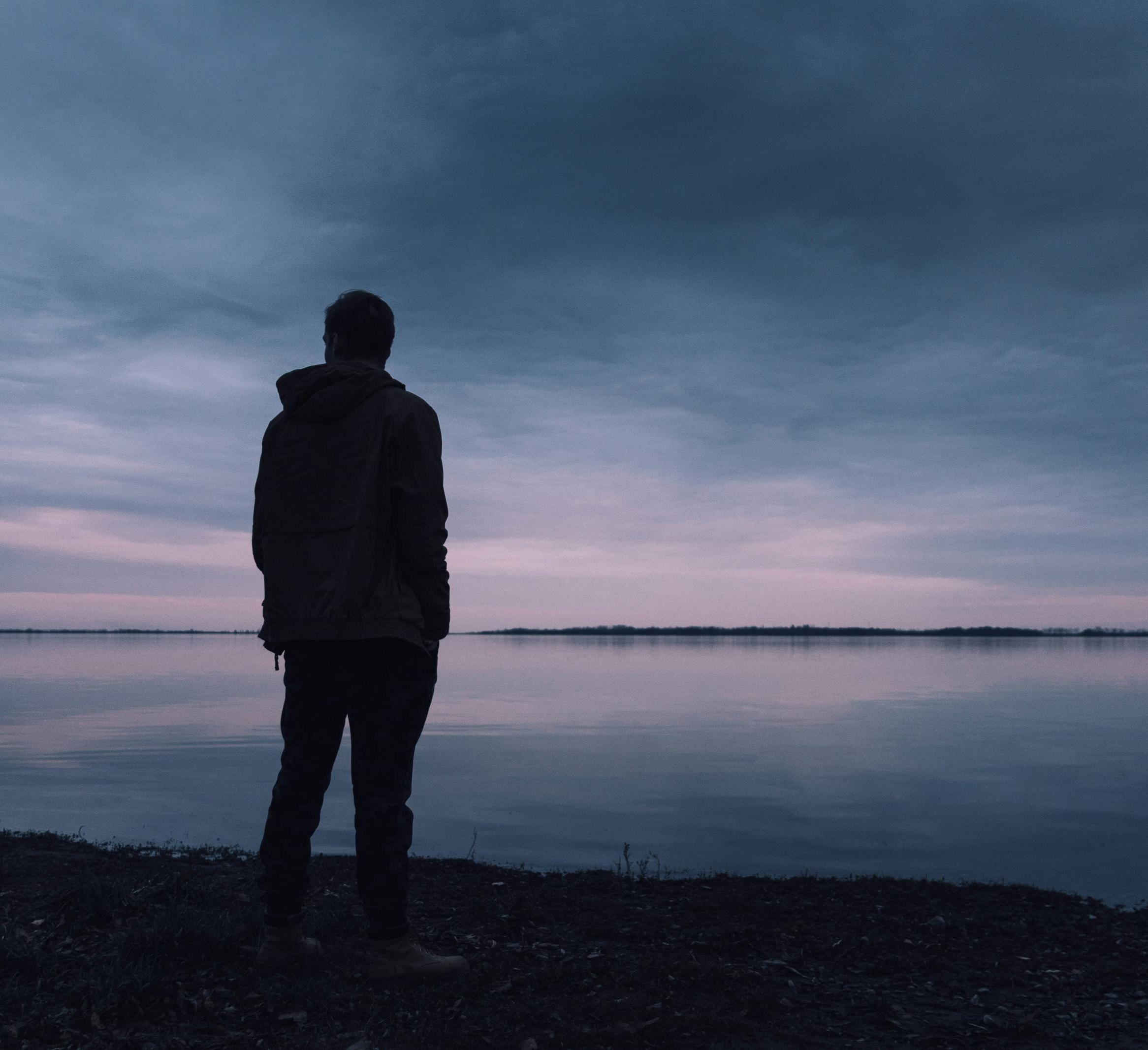 A person stands alone and looks at a lake