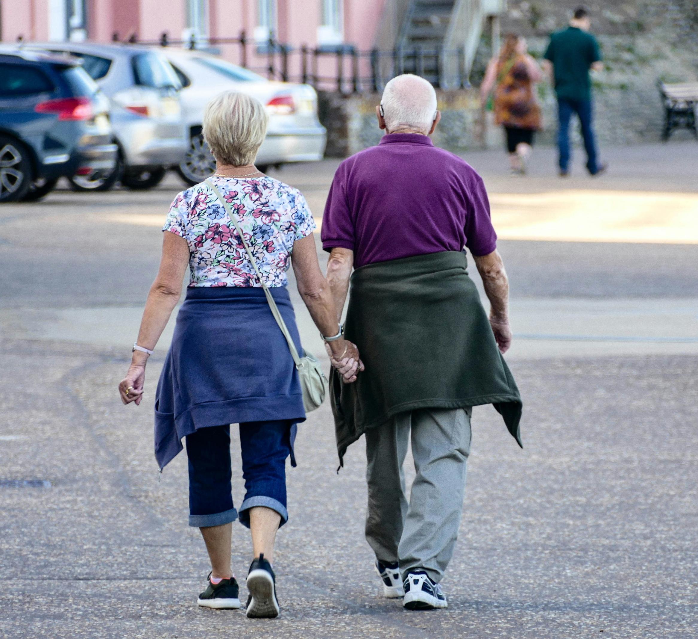an older adult couple walks hand in hand