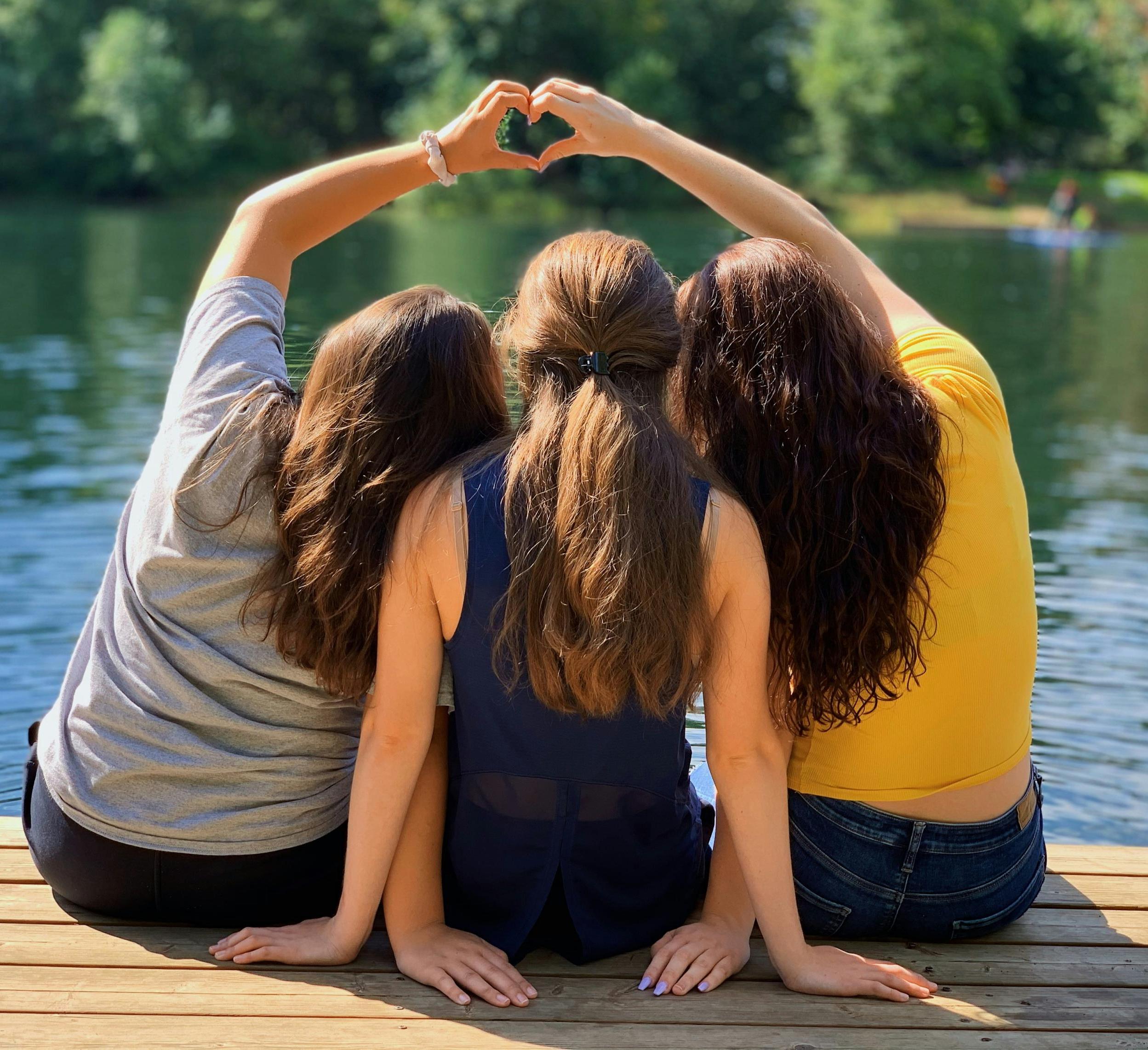 three girls sit together on a dock