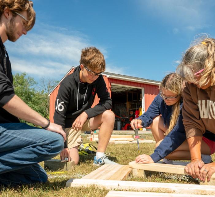 Cornell Cooperative Extension Jefferson County community school coordinator Donna Jean Coleman (right) helps LaFargeville Central School students Alexander Moore (far left), Samuel Duffany and Ella Hunneyman screw together boards on a flower box they built for a student-led community beautification project.